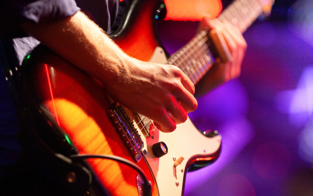 一個人在舞台上彈奏電吉他的特寫鏡頭，背景有發光的舞檯燈光。