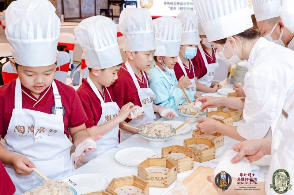 一群戴著廚師帽、穿著圍裙的孩子們正在兩位成年廚師的指導下學習包餃子。桌上擺放著各種餃子材料和蒸籠。