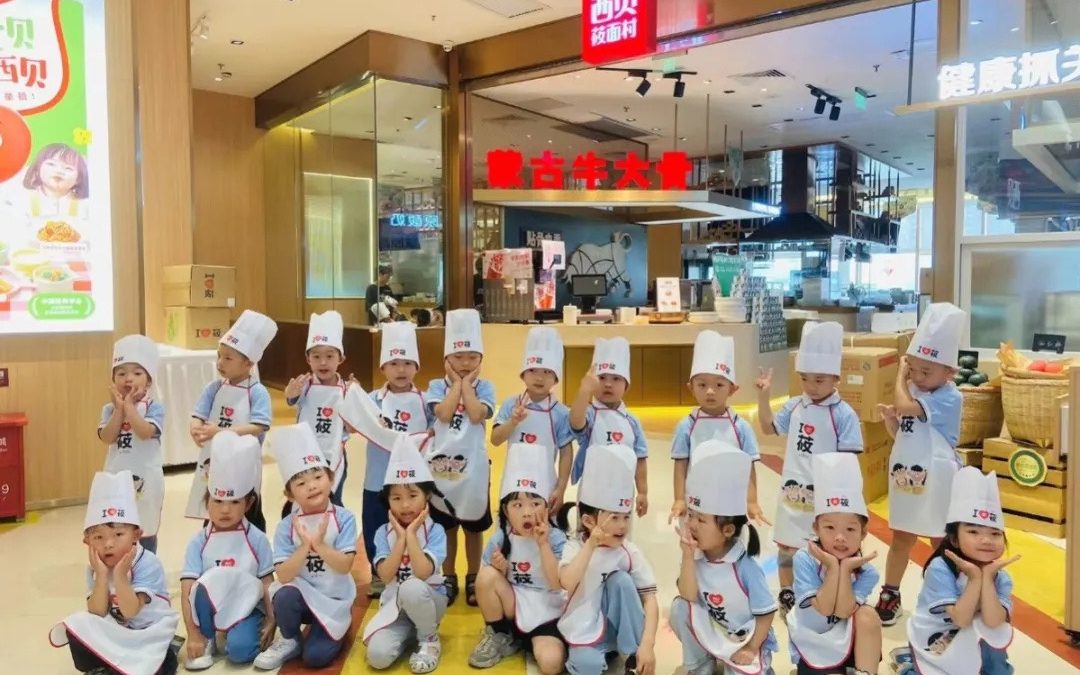 一群戴著廚師帽、穿著圍裙的孩子在餐廳入口附近的購物中心擺姿勢。有些人坐著，有些人站著，所有人都微笑著並做出各種手勢。