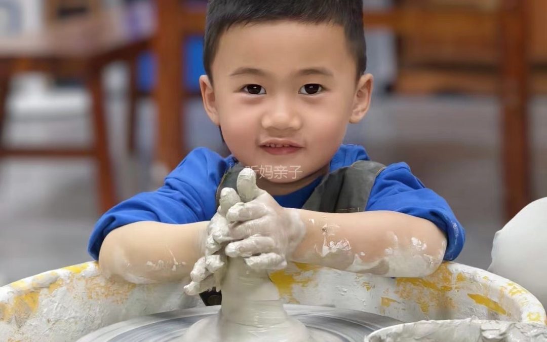 一個小孩正在陶輪上專心地塑造黏土。他的手上沾滿了濕黏土，背景中可以看到各種陶器和材料。