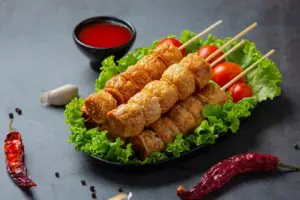 烤肉串放在生菜上,搭配櫻桃番茄,配一小碗紅色蘸醬和乾辣椒。.