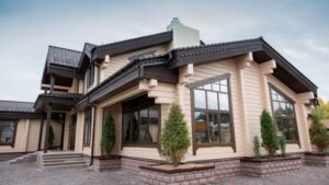 一棟現代化的兩層樓房,有大窗戶、米色壁板、深色飾邊,以及鋪好的車道,外圍還種有小樹。.