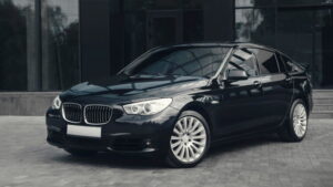 一輛黑色 BMW 轎車停在一棟現代玻璃建築前的鋪面上。.