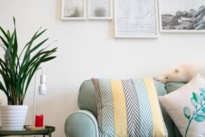 粉綠色的沙發配上圖案鮮明的坐墊,側桌上放著盆栽,白色牆面上掛著有框的藝術品。.